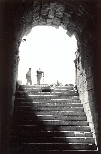 black and white photograph of an steps leading up to an archway, with two men seen from behind