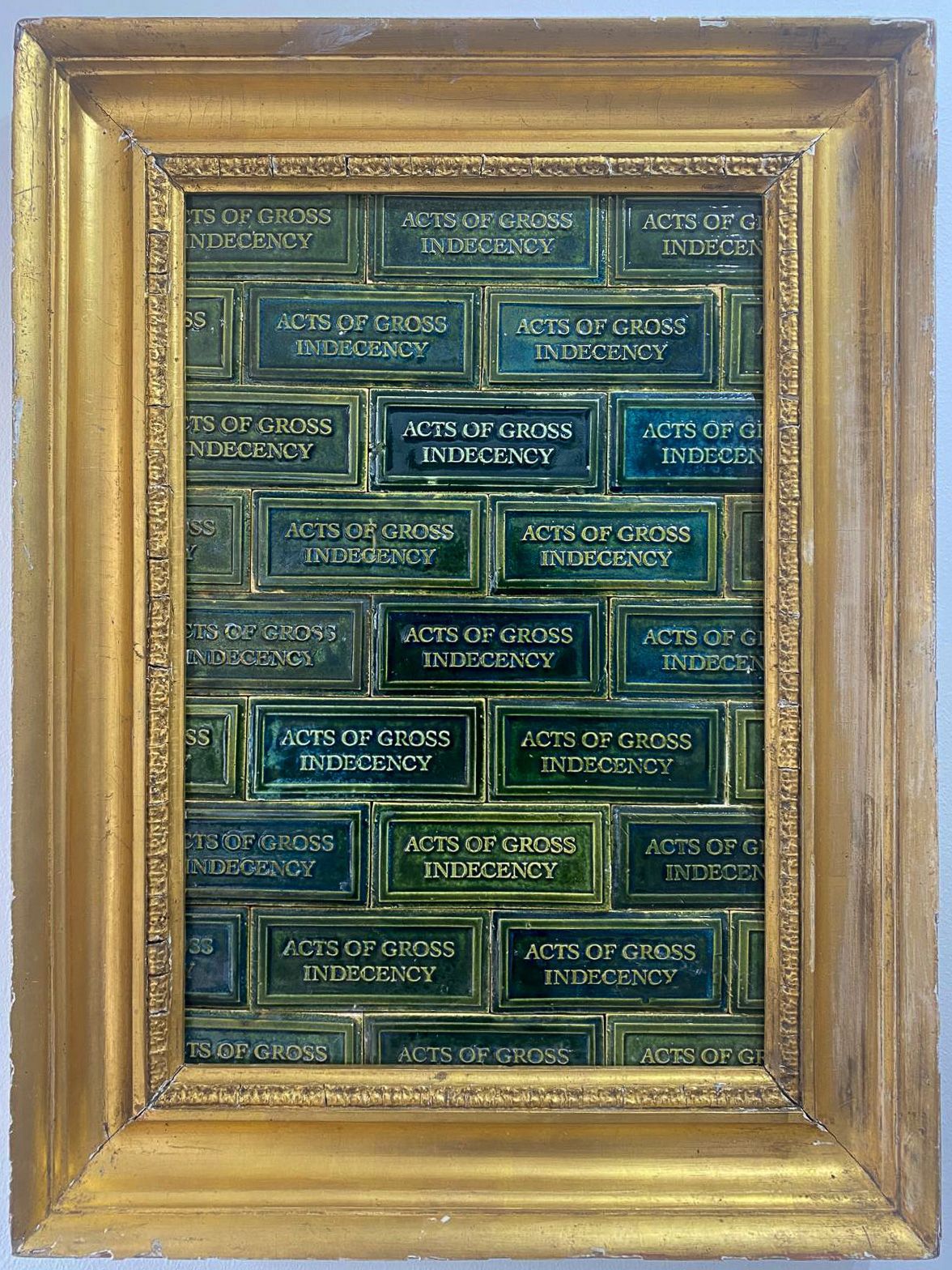 Green subway tiles, with the words 'Acts of Gross Indecency', within a frame. Artwork by Mark Mann.