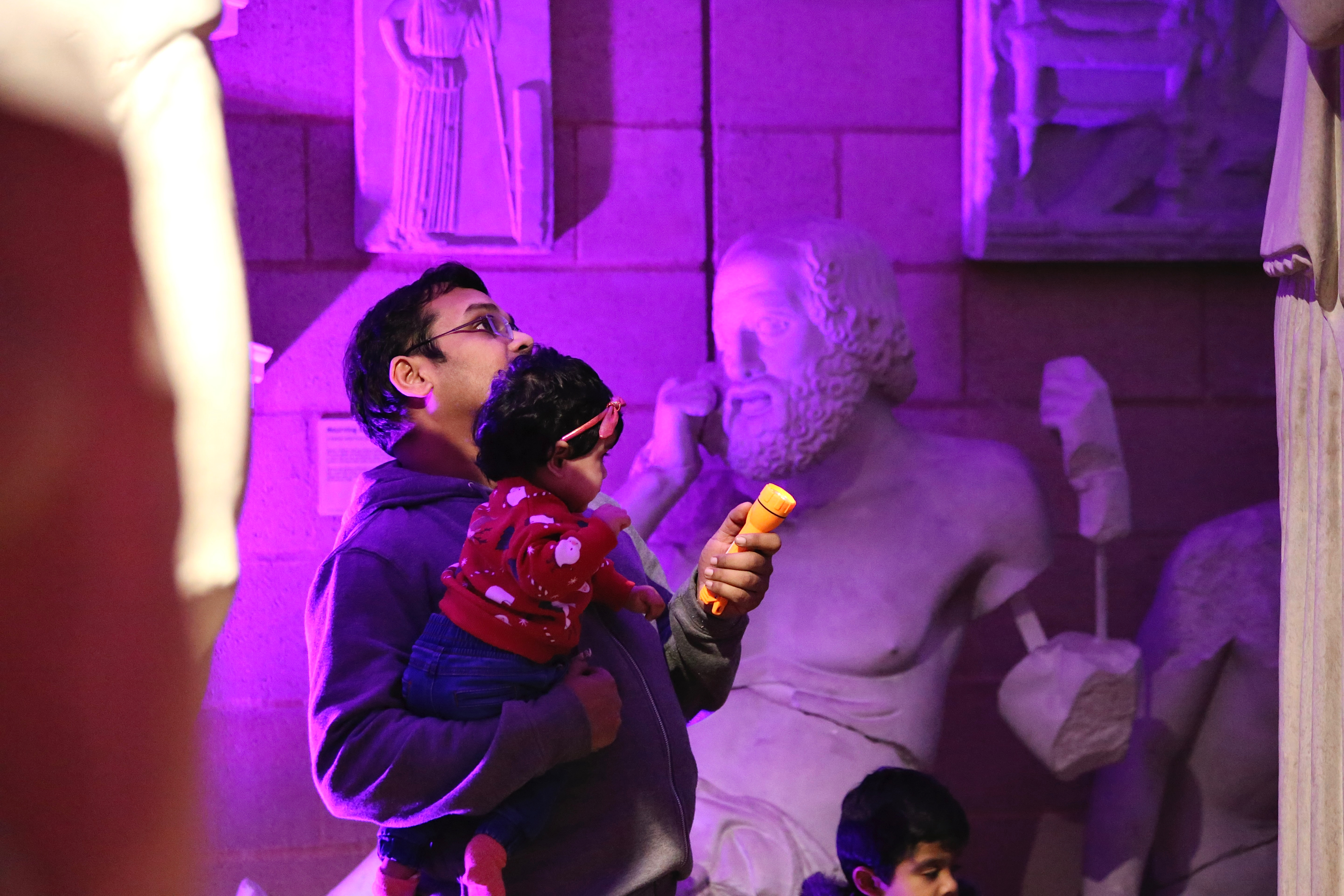 Father and daughter looking up at a large statue, holding a torch.