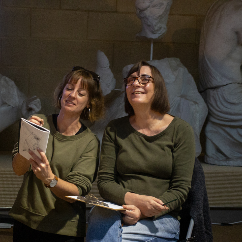 A brunette woman helping another brunette woman to sketch in a museum gallery