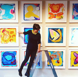 the artist on a ladder, in front o brightly coloured art works