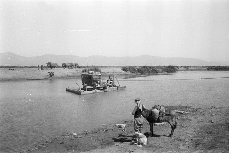 black and white photograph of a raft on a river and a man and donkey on the shore