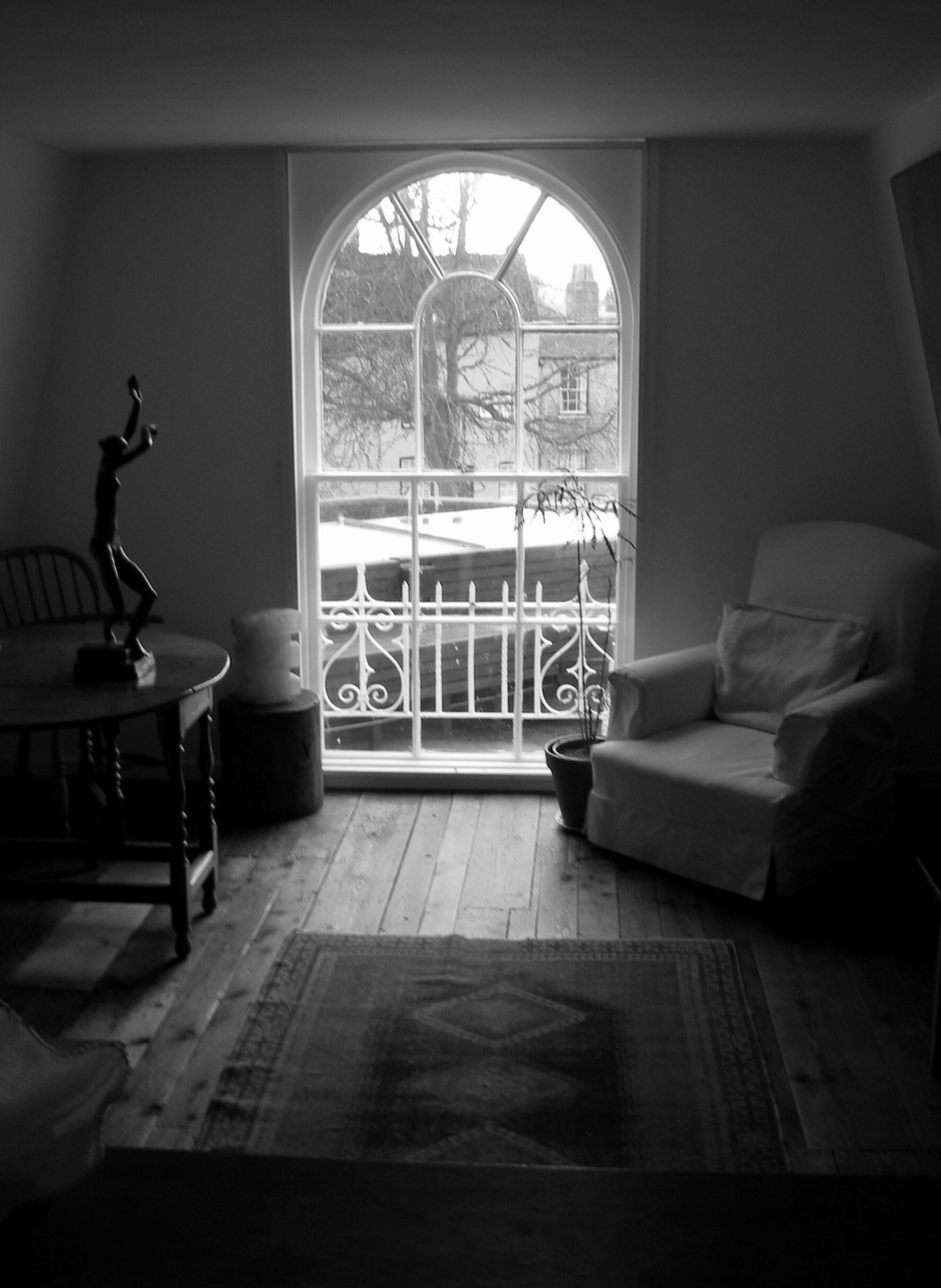 black and white image of a window with an armchair and a dancing figure on a table