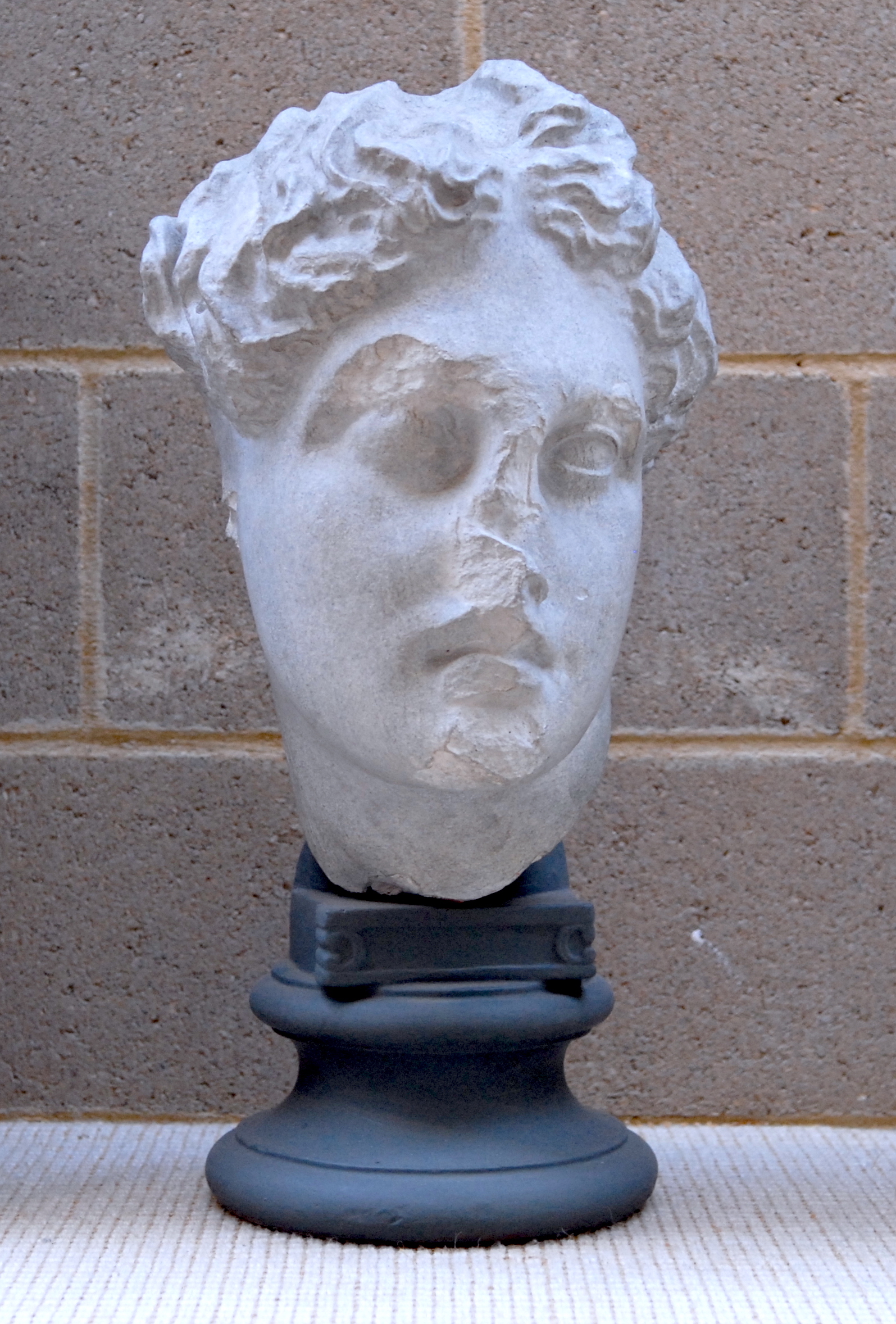 sculpted head of apollo, head bent to one side, with hair in little knots on top of head