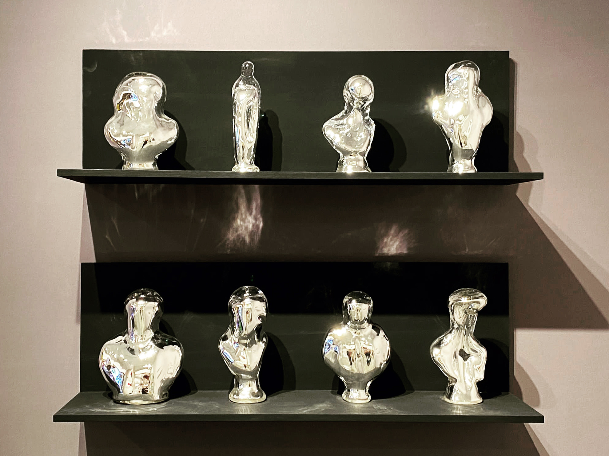 distorted busts made of silvered glass, on black shelves
