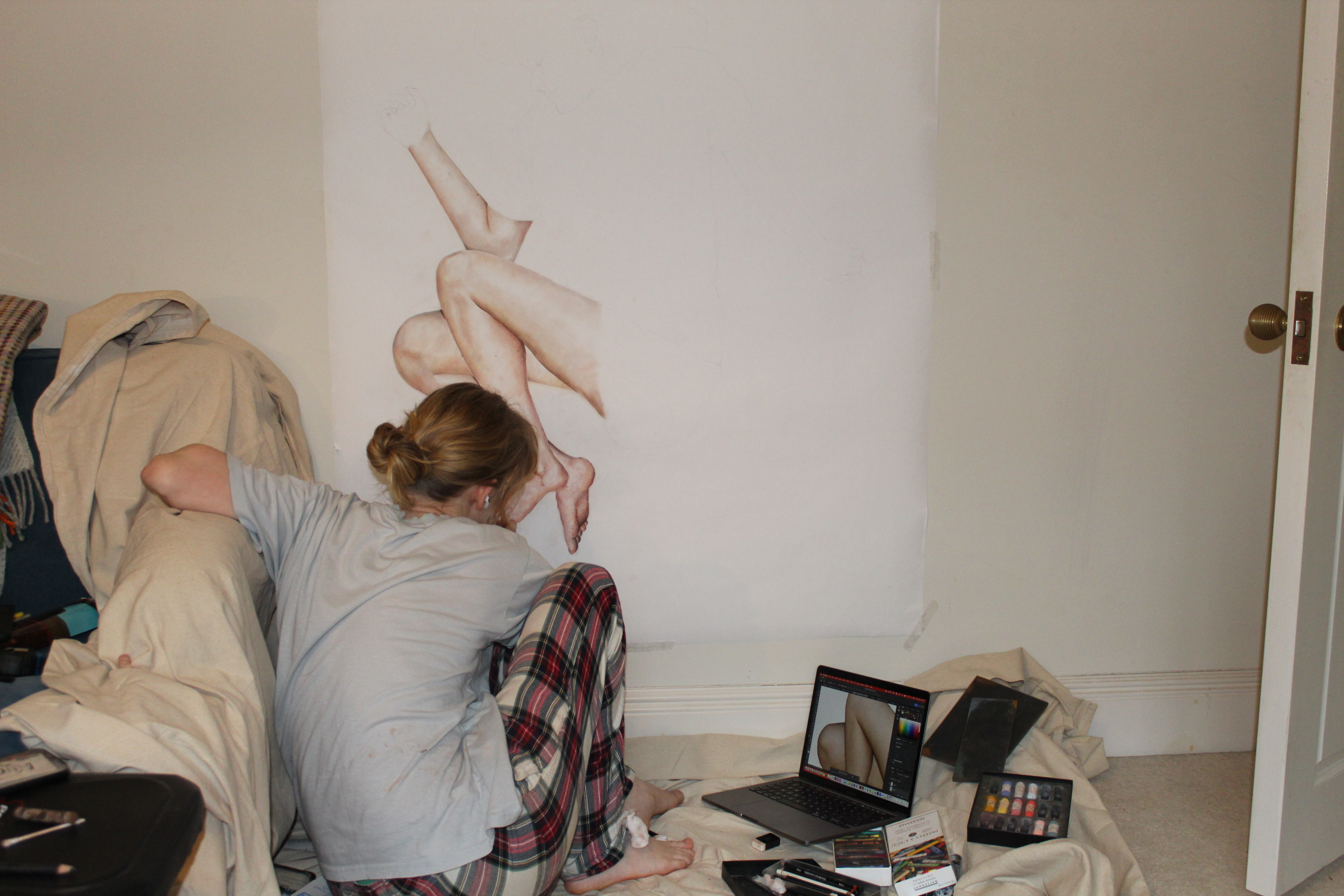 a student paints a canvas, working from a photograph of entwined bodies on her laptop screen