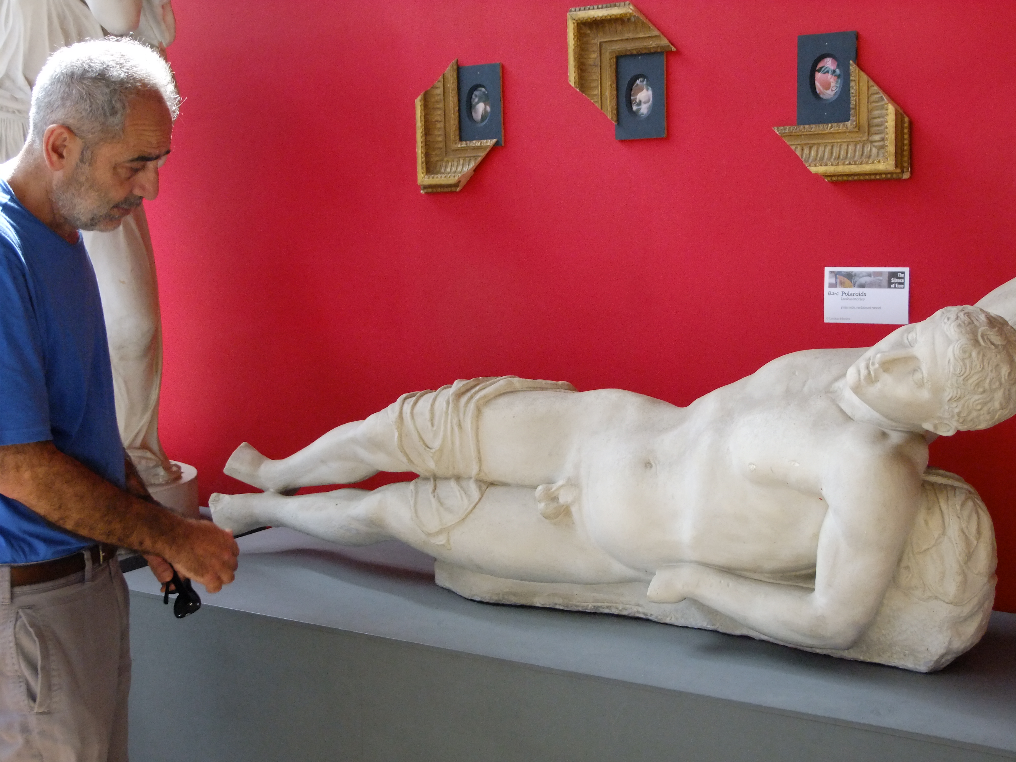 A Syrian man stands mournfully looking at a sculpture of reclining young man