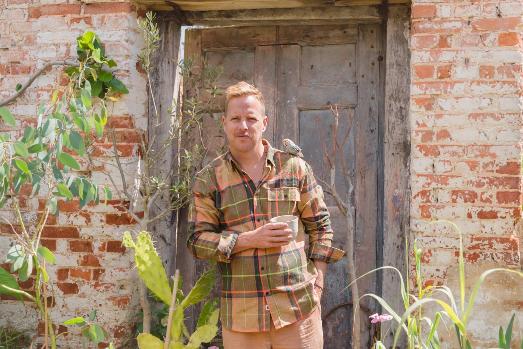 Artist Mark Mann standing outside his studio, with a bird on his shoulder