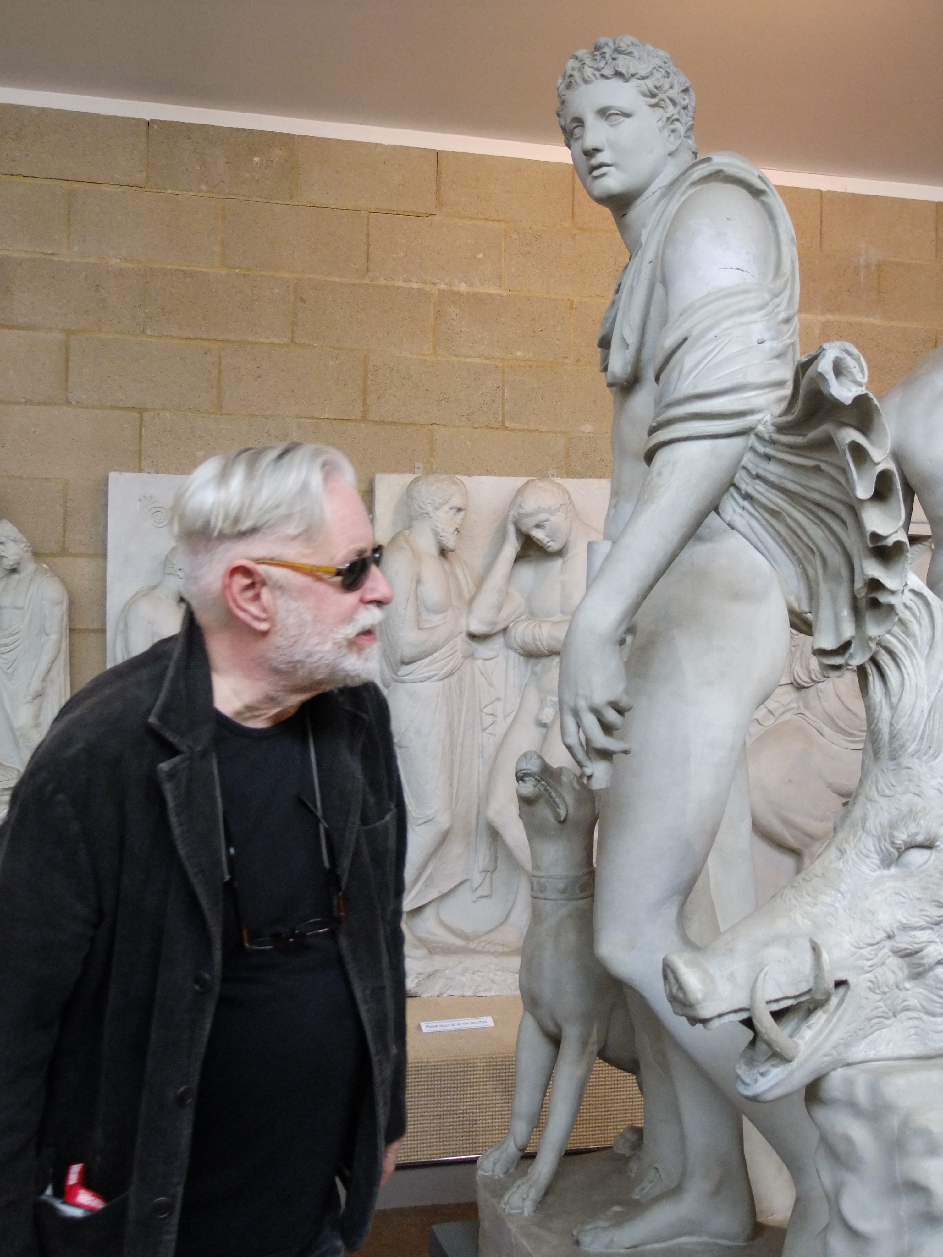 a man in sunglasses looks at a sculpted young man with boar's head and dog