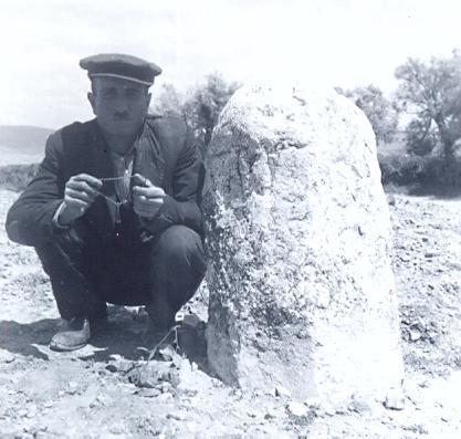 black and white photo of a local Turkish man kneeling nex tot a standing stone