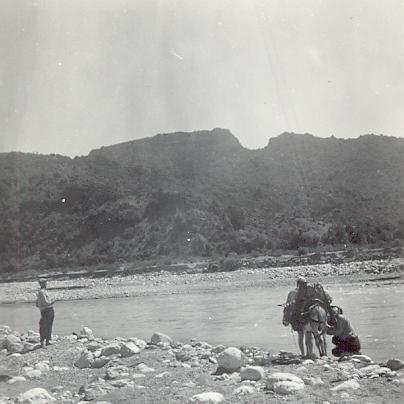 black and white photographoof a donkey and two men next to a body of water