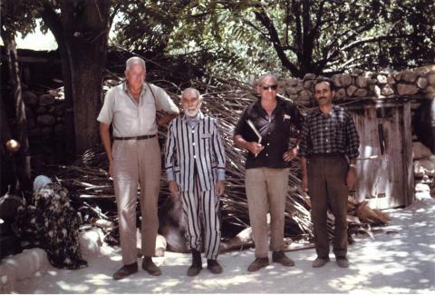 colour photo of four men in front of trees and a stone wall