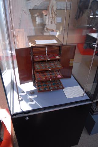 a display cabinet with an open wooden box of drawers with coins