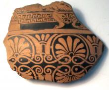 broken piece of Greek pottery, with black patterns on red background' width=