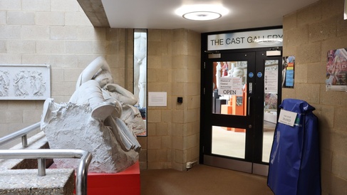 large cast of a reclining figure next to a black door with windows on a landing