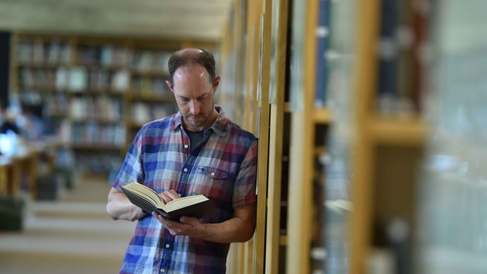 a man in a plaid shirt reads a book in the library