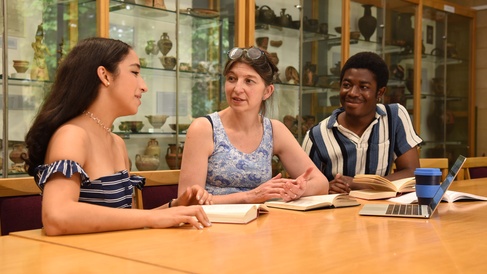two students sit at a table with a supervisor in a room full of ancient pots