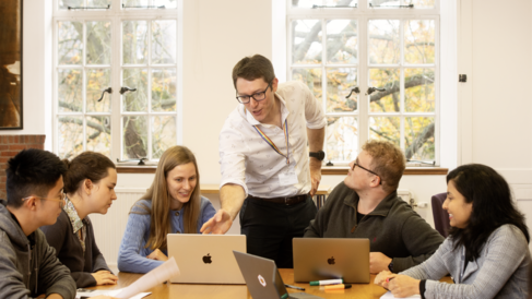 A teacher helps a group of students on laptops