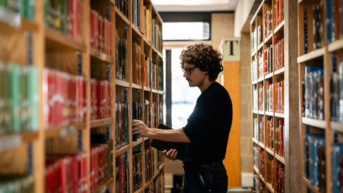 a young man pulls a book off the shelf in the classics library