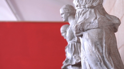 three sculpted women against a red background