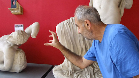 Issam Kourbaj reaches out to one of the dying Niobid statues, against a red wall 