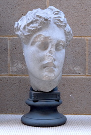sculpted head of apollo, head bent to one side, with hair in little knots on top of head