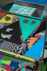 Three glass shelves, with layered coloured mountboard shapes, photographic images and ancient sherds