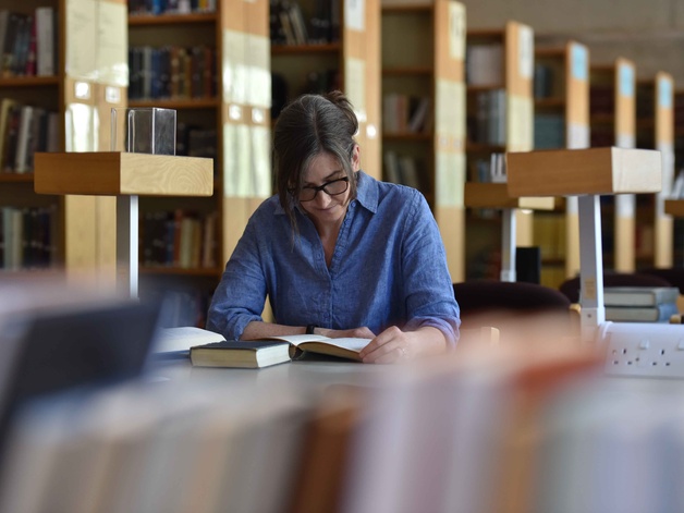 a woman in a blue shirt sits reading a book in the library