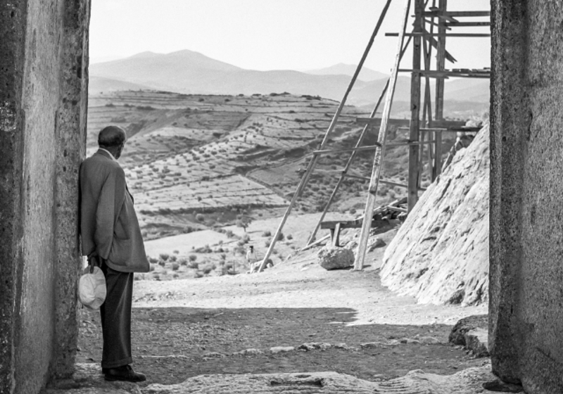 Alan Wace, a tall man in a blazer, looks out at the landscape of Mycenae beyond the Lion Gate